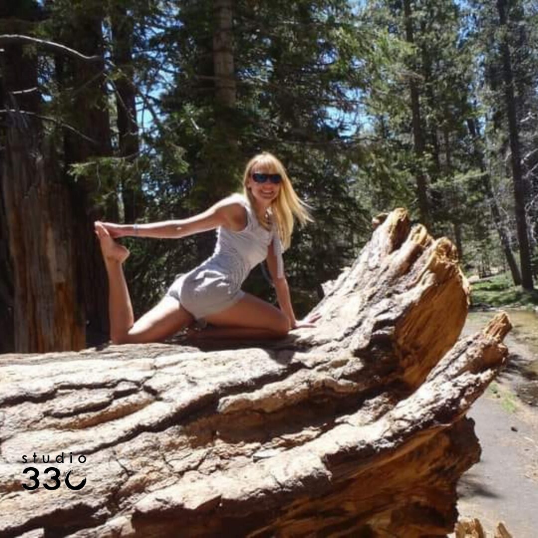 Monique on a fallen tree outdoors performing a yoga pose